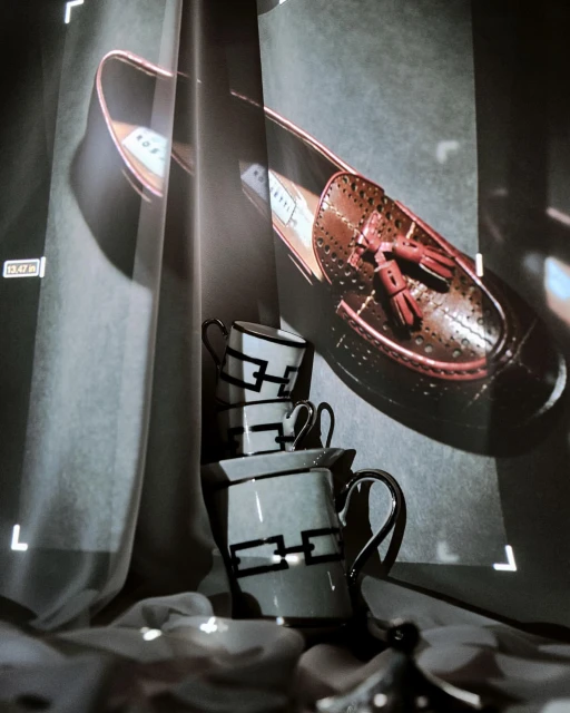 Artistic display of a brown leather loafer with tassels alongside a stack of teacups, creatively positioned against a textured backdrop.