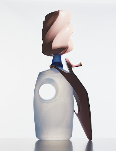 Conceptual still life with a laundry detergent bottle, high heel shoe, and decorative object against a bright white background in studio.