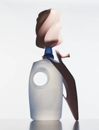 Conceptual still life with a laundry detergent bottle, high heel shoe, and decorative object against a bright white background in studio.