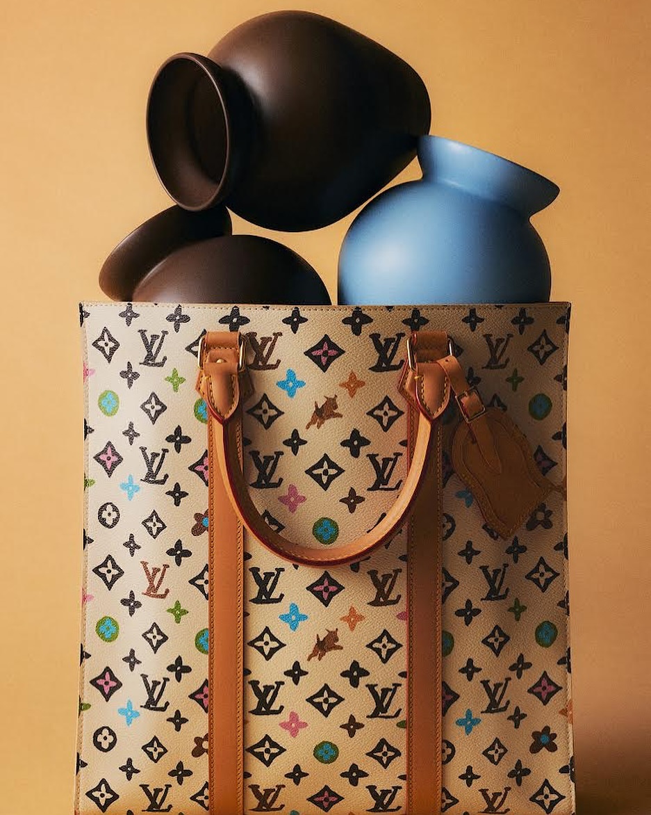 Monogrammed Louis Vuitton tote bag with brown and blue ceramic vases in a studio setting against a gradient peach-colored background.