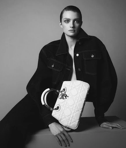 Black and white fashion portrait of a woman in denim jacket holding a Lady Dior handbag in a photo studio setting. 
