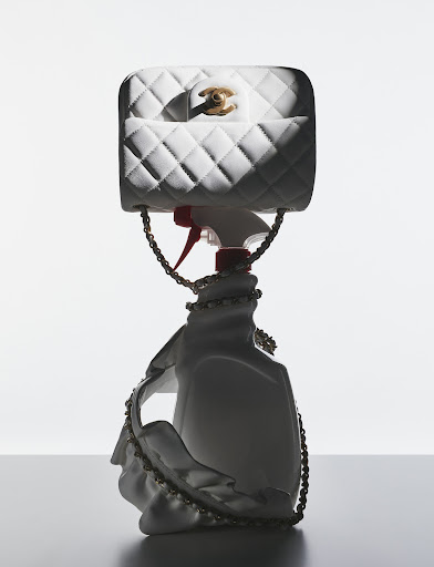 White quilted Chanel handbag perched atop a spray bottle, artfully arranged in a product shot with soft lighting and clean background.