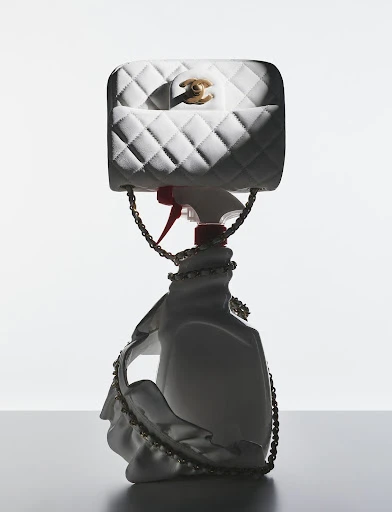 White quilted Chanel handbag perched atop a spray bottle, artfully arranged in a product shot with soft lighting and clean background.