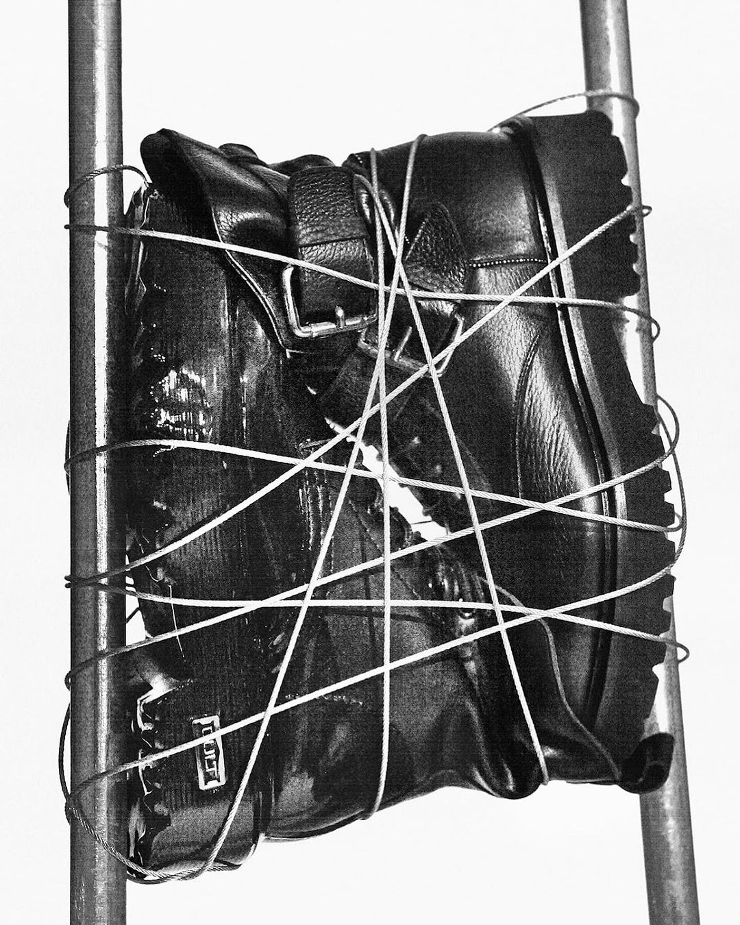Close-up of a black leather boot, secured by a white string, against a white background and metal support poles.