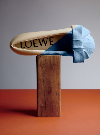 Stylized fashion product shot of a beige shoe on a wooden block with a sky-blue textured treatment, in a studio setting with warm lighting.