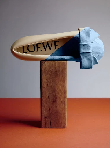 Stylized fashion product shot of a beige shoe on a wooden block with a sky-blue textured treatment, in a studio setting with warm lighting.