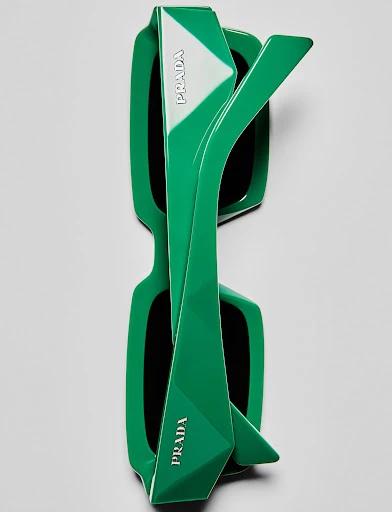 Top-down studio shot of green Prada sunglasses with white logo detailing, showcasing modern design and contrasting colors against a neutral background.