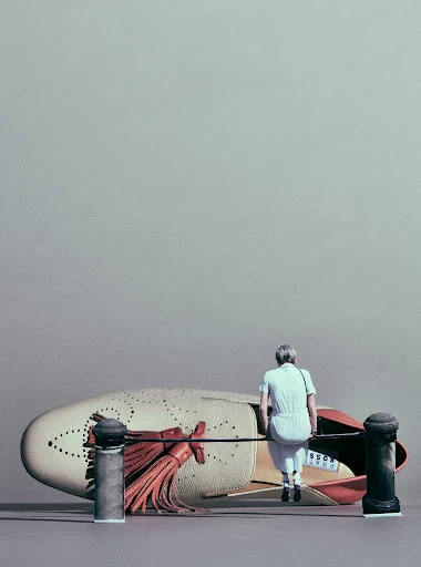 Miniature woman in jumpsuit sitting on a metal pipe near a giant loafer shoe, with two black posts on a light gray background.