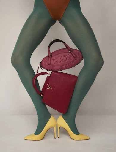 Fashion shot of a model's legs wearing green hosiery and yellow heels with a Tod's purse and a red Louis Vuitton handbag.