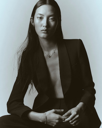 Portrait of an east asian model wearing a black blazer and delicate jewelry against a plain light background