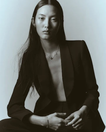 Portrait of an east asian model wearing a black blazer and delicate jewelry against a plain light background