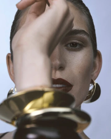 Close-up portrait of a woman with dark lipstick and gold hoop earrings, holding her arm up in the foreground by Marco Gazza.