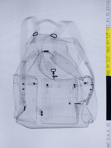 X-ray image of a backpack, showing internal compartments and straps against a white background with calibration text along the side.