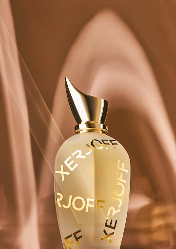 Elegant perfume bottle with a gold cap against a soft brown background, branded with XERJOFF lettering, product photography.