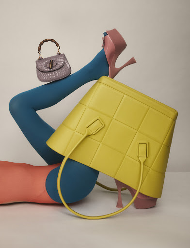 Fashion shot featuring a woman's legs wearing blue tights and platform heels, showcasing a yellow leather purse and purple handbag.
