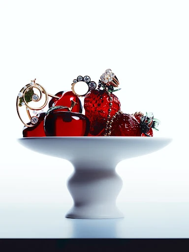 Elegant jewellery rings displayed on glazed cherries and strawberries, artfully arranged on a glossy white pedestal against white.
