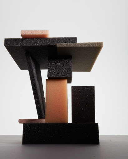 Abstract architectural sculpture features geometric shapes in black, beige, and peach foam, casting soft shadows in a modern art arrangement.