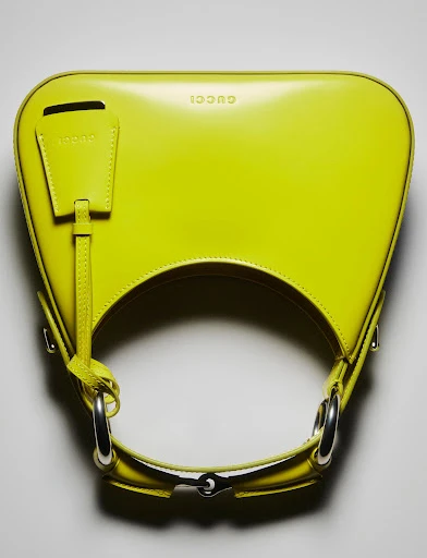 Close-up of a vibrant yellow Gucci handbag featuring silver hardware. The purse is displayed against a neutral backdrop.