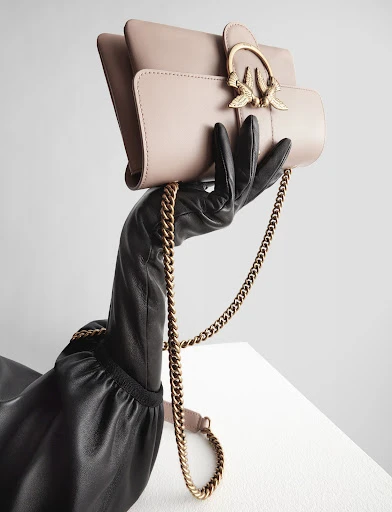 Elegant handbag display: A gloved hand presents a blush-toned purse with golden chain against a clean, minimalist background, fashion-forward.