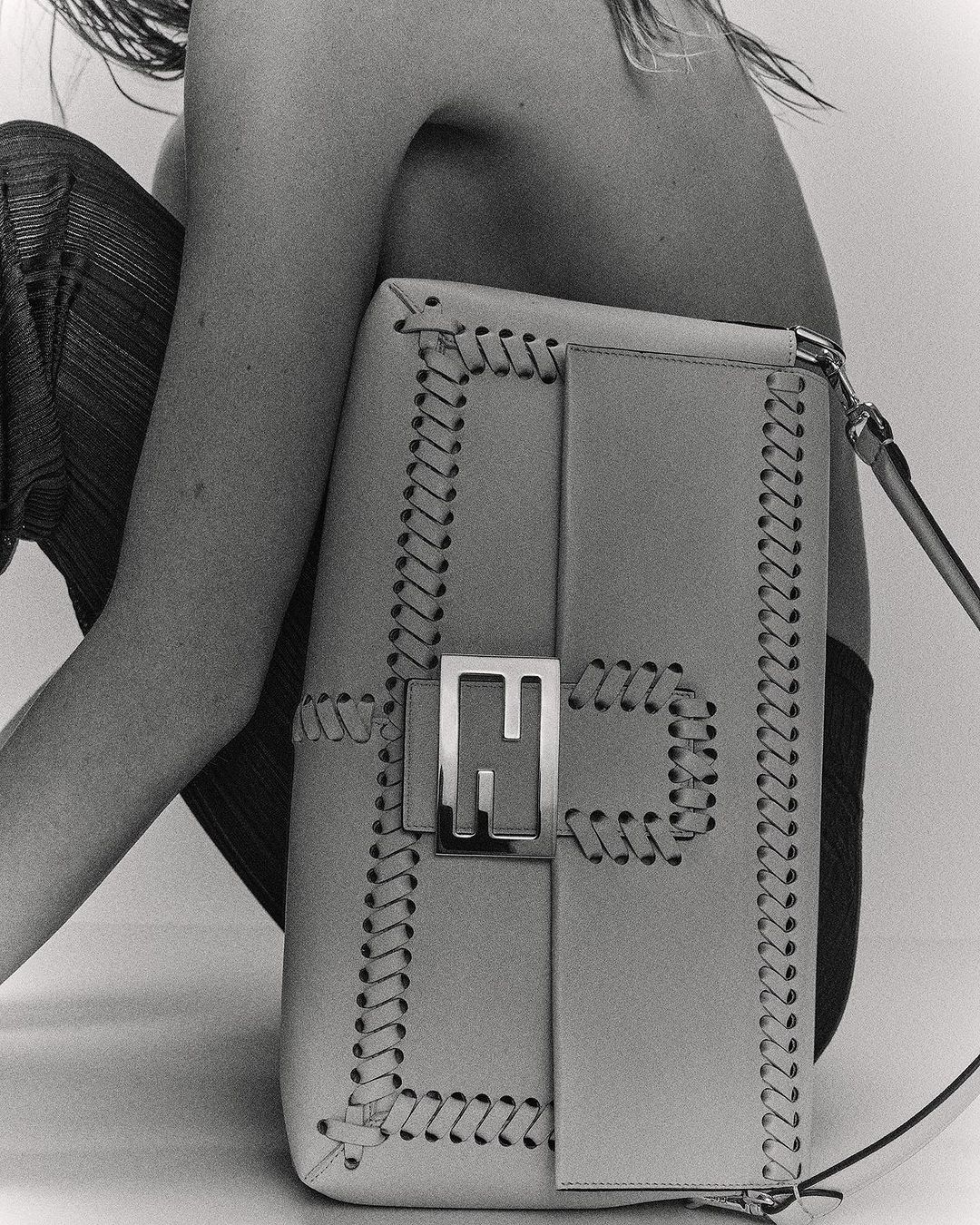 Fashion shot showcasing a Fendi handbag with a metal logo, set against a neutral backdrop with a partially visible human figure.