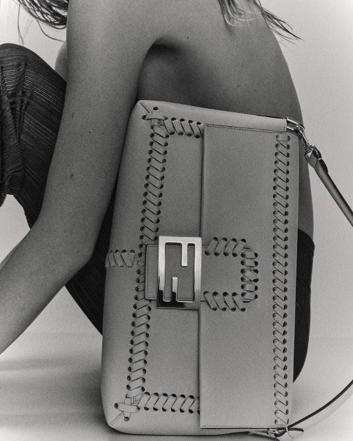 Fashion shot showcasing a Fendi handbag with a metal logo, set against a neutral backdrop with a partially visible human figure.