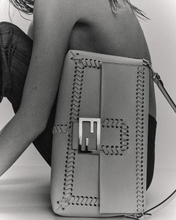 Fashion shot showcasing a Fendi handbag with a metal logo, set against a neutral backdrop with a partially visible human figure.