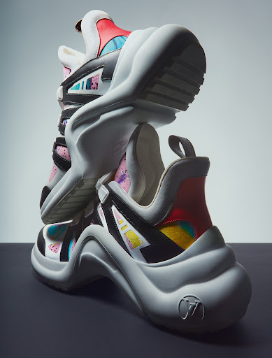 Two chunky designer sneakers stacked vertically against a split white and grey studio background shot by Marco Gazza