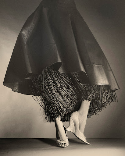 Close-up of a model wearing a flared leather skirt with fringed hem and wedge shoes by Marco Gazza