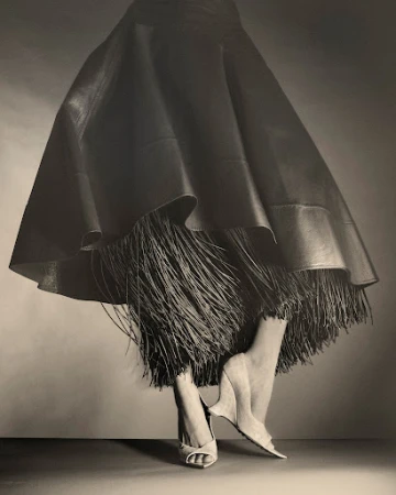 Close-up of a model wearing a flared leather skirt with fringed hem and wedge shoes by Marco Gazza