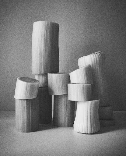 Monochromatic still life of stacked leeks with cut stalks, creating an abstract architectural form against a neutral gray backdrop.