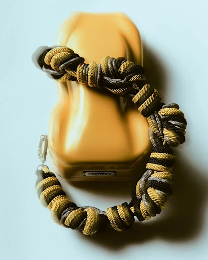 An abstract shot of a yellow Ferrari model car with a decorative knotted bracelet coiled around it on a white surface, high angle.