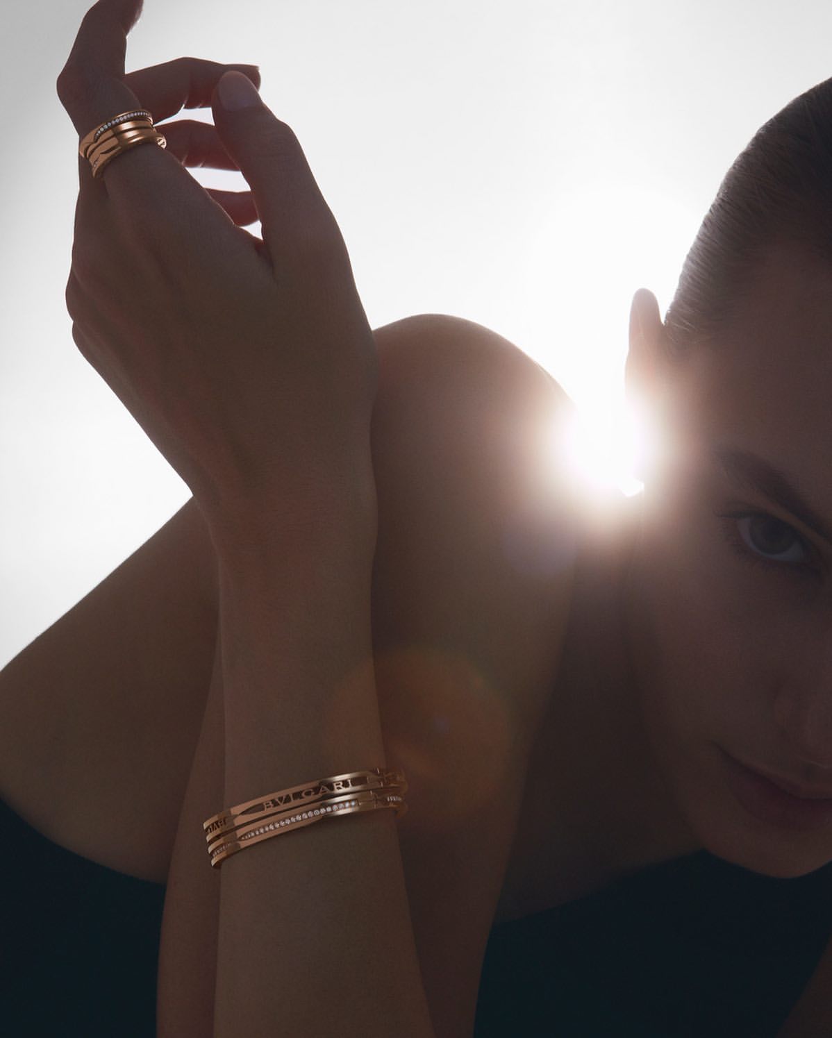 Close-up shot of a woman with light skin wearing rose gold jewelry including a bangle bracelet and rings, with bright lighting.