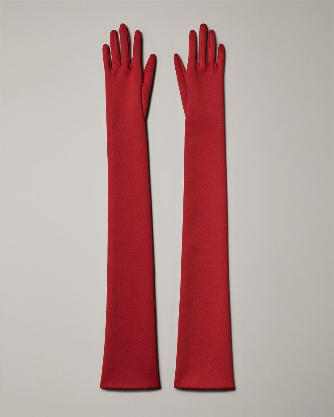Pair of long red opera gloves on a neutral background. Fashionable and elegant evening gloves.