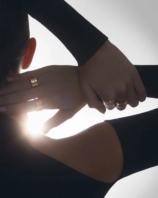Close-up of a woman's hands with gold rings, backlit against a bright white background, showcasing jewellery and fashion.