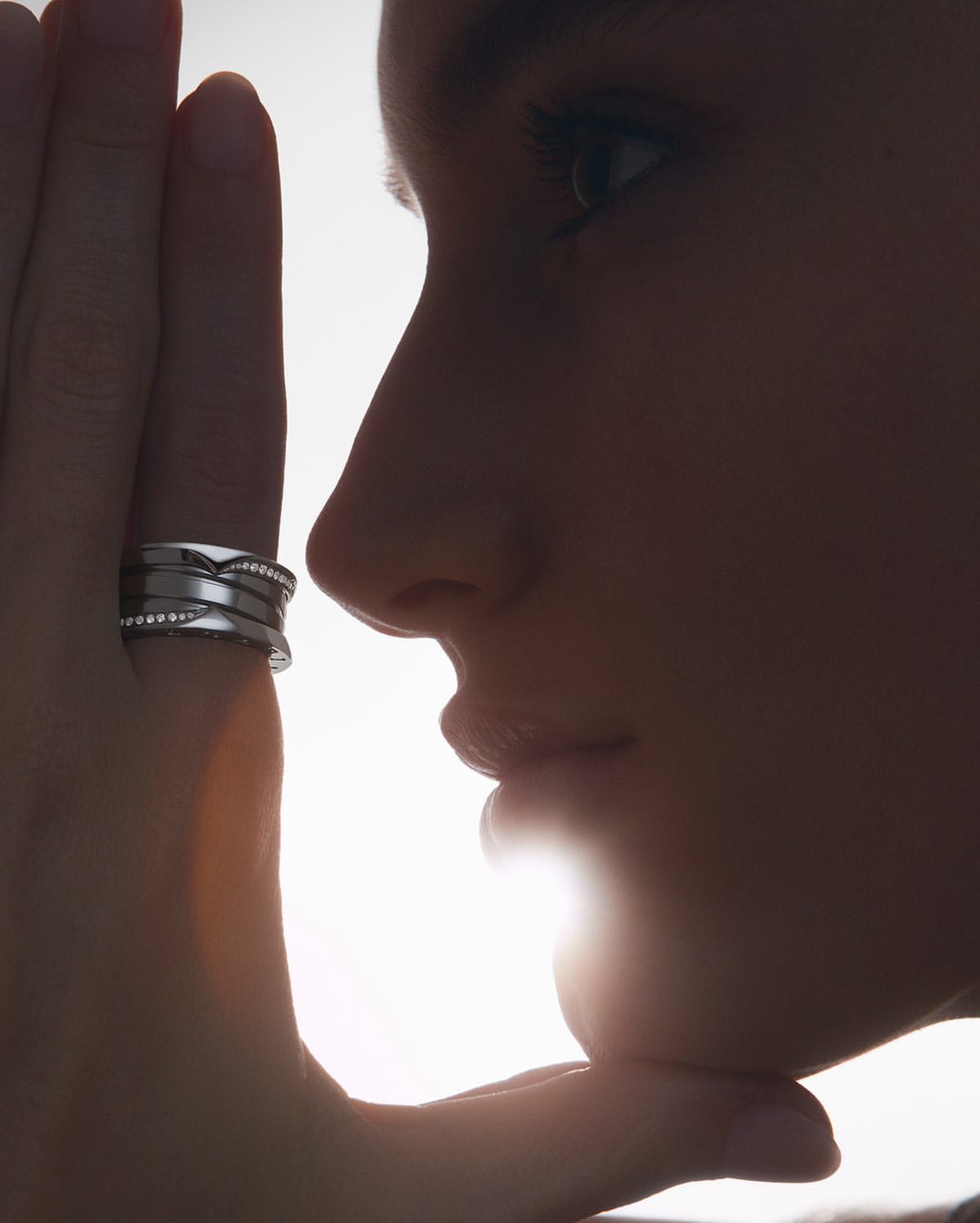 Close-up of a woman's face in silhouette, with a silver ring on her finger against a bright white background, showcasing jewelry and beauty.