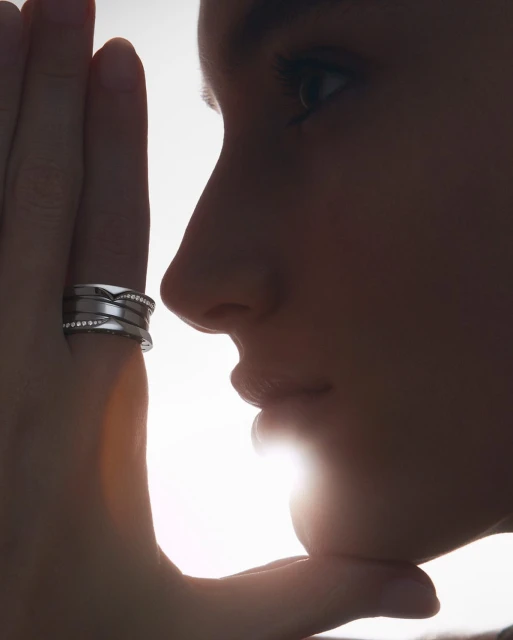 Close-up of a woman's face in silhouette, with a silver ring on her finger against a bright white background, showcasing jewelry and beauty.