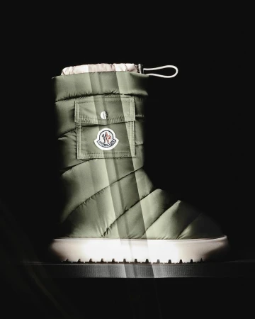 Olive green quilted boot with white sole and Moncler logo detail, captured in a dark, spotlighted setting. Product shot.
