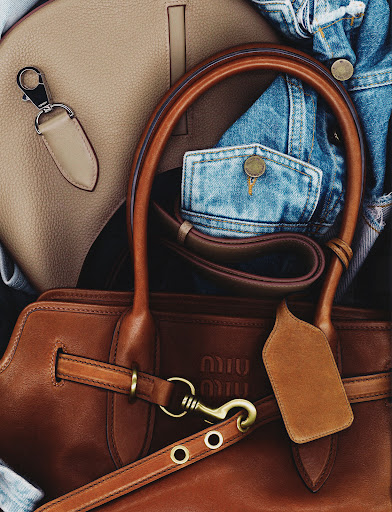Close-up of a brown leather Miu Miu handbag with light-brown leather handbag and a blue denim jacket in the background.