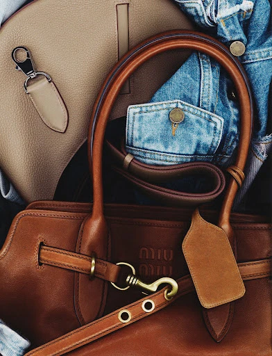Close-up of a brown leather Miu Miu handbag with light-brown leather handbag and a blue denim jacket in the background.