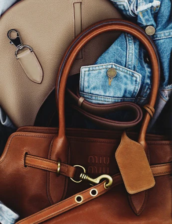 Close-up of a brown leather Miu Miu handbag with light-brown leather handbag and a blue denim jacket in the background.