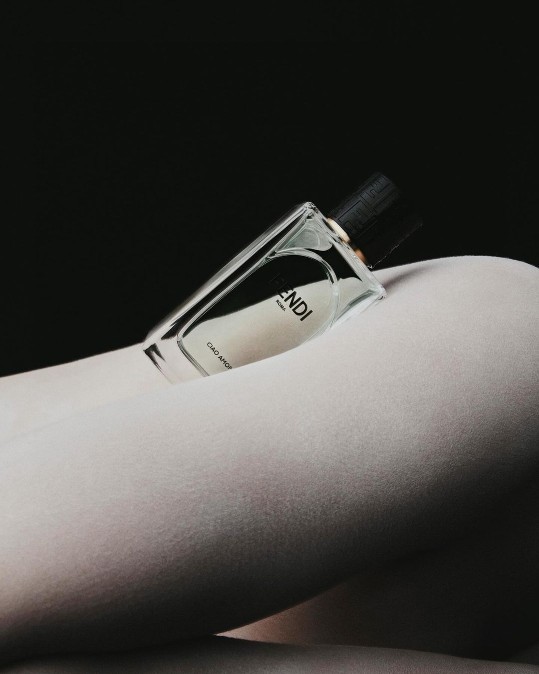 Fendi perfume bottle resting on a person wearing white tights against a dark background