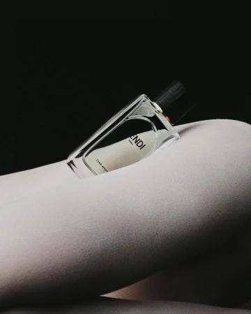 Fendi perfume bottle resting on a person wearing white tights against a dark background