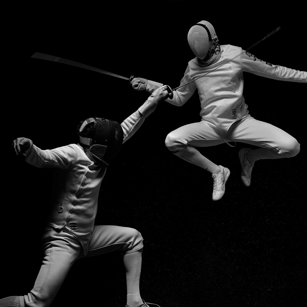 Two fencers engaged in a match, wearing protective gear and holding swords, set against a stark black background in a dynamic black and white image.