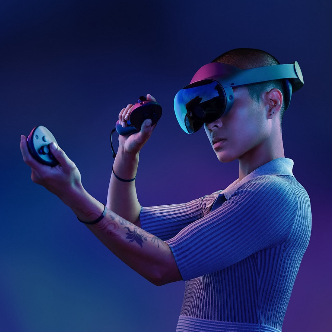 Young adult wearing VR headset and holding controllers against blue and purple background. Technology and gaming concept.