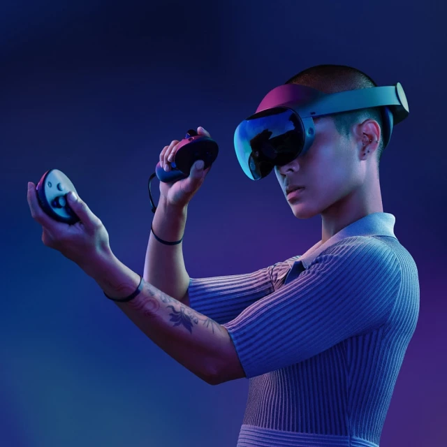 Young adult wearing VR headset and holding controllers against blue and purple background. Technology and gaming concept.