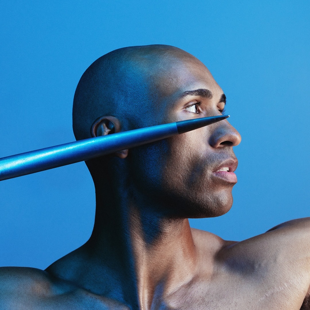 Bald adult male with spear near his face in a studio shot. Head and shoulder view on blue backdrop. Sports concept.