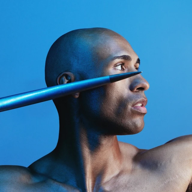 Bald adult male with spear near his face in a studio shot. Head and shoulder view on blue backdrop. Sports concept.