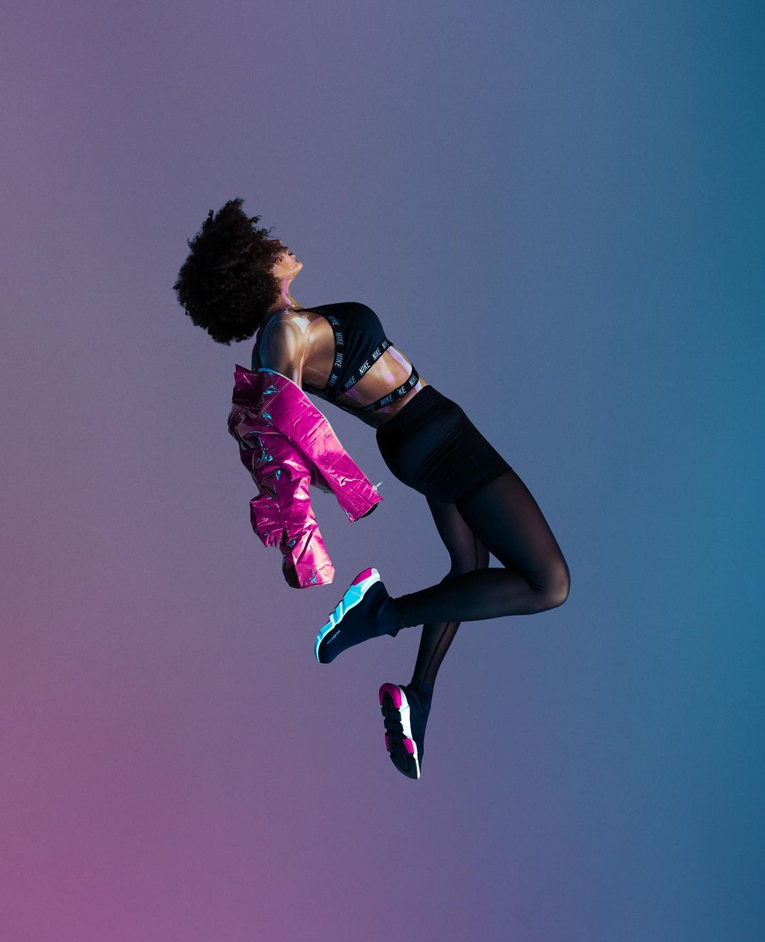 An athletic African American woman suspended in mid-air wearing workout clothes and a bright pink jacket against a gradient background.