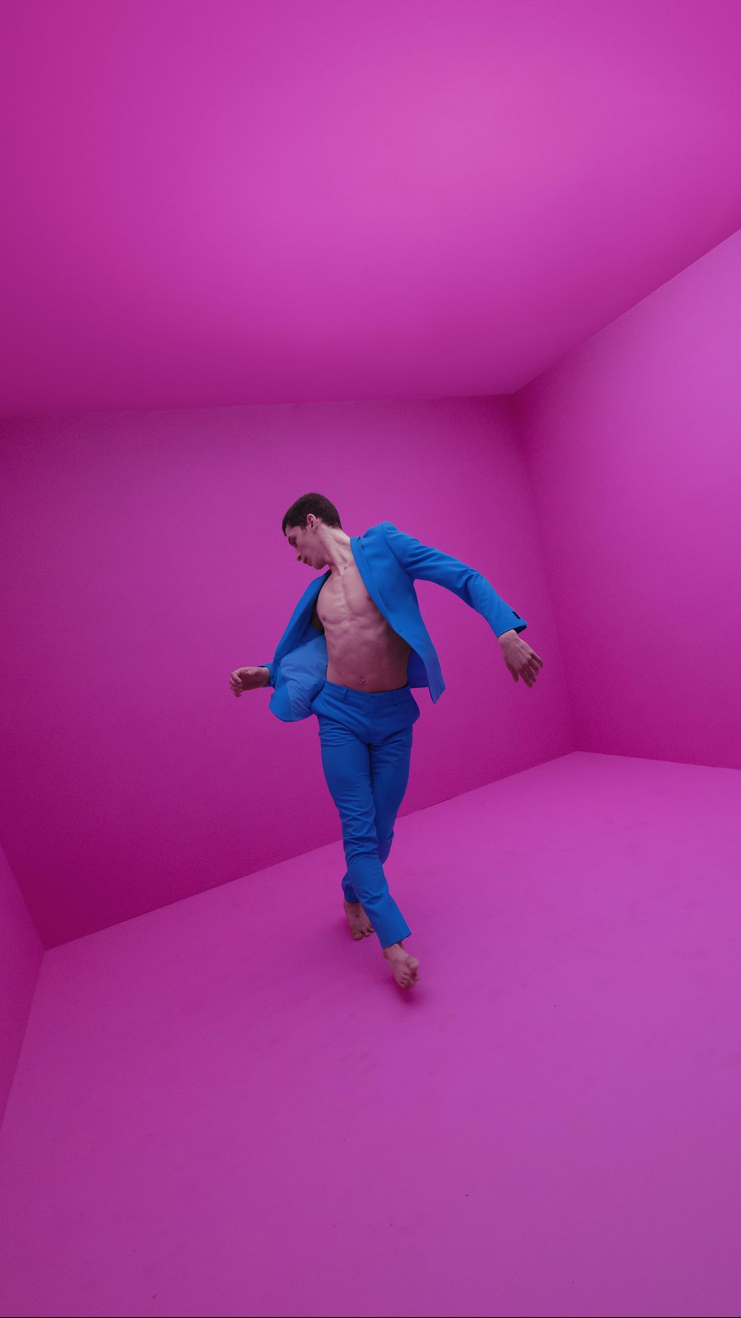 Athletic man in blue suit posing in pink room. Solo male fashion and artistic expression with bright colors and bare chest.