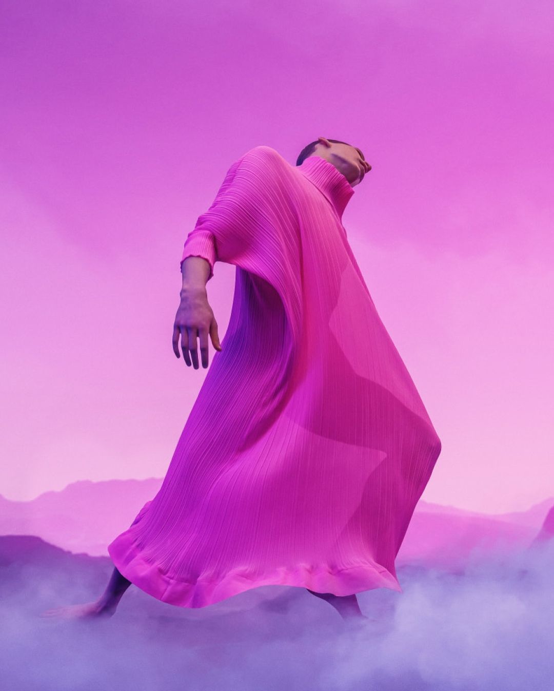 Person in long pink pleated dress striking a pose in front of pink sky and landscape with fog. Fashion editorial photography.